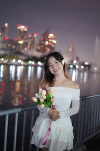 Portrait of young woman standing against illuminated string lights