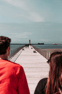 Rear view of people on railing by sea against sky