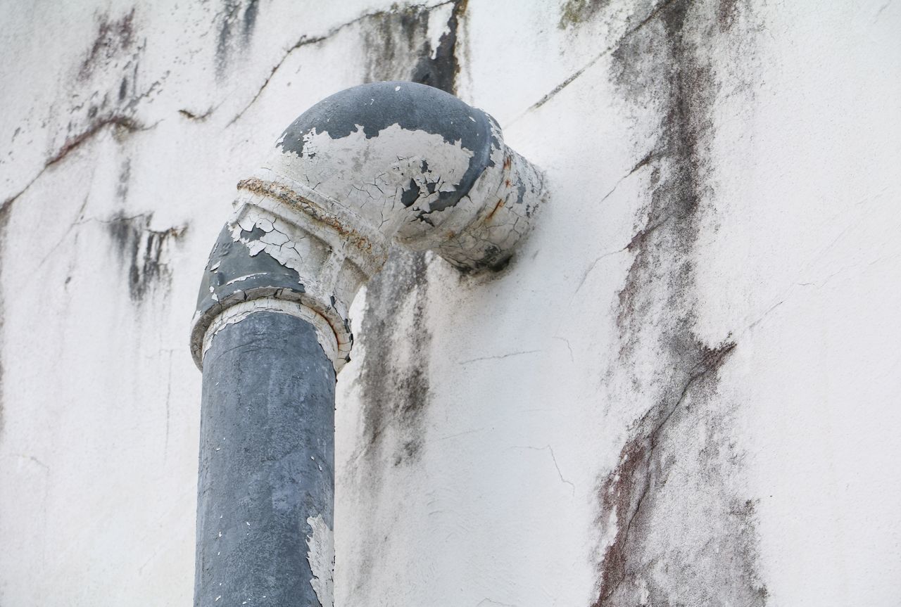 LOW ANGLE VIEW OF PIPE ON WALL WITH WHITE BUILDING