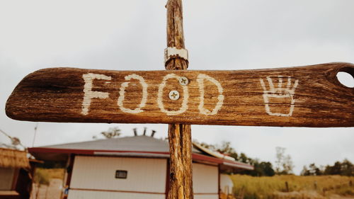 Close-up of food sign on wooden post against sky