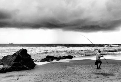 Rear view of man walking at beach against cloudy sky