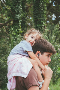 Brother carrying sister on shoulders in forest