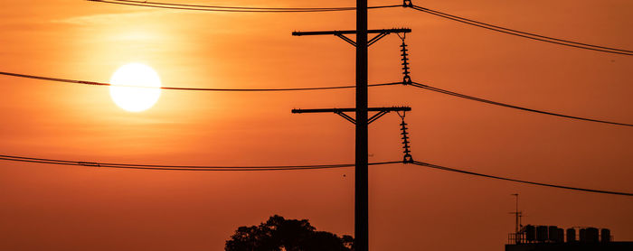 Low angle view of electricity pylon against sky during sunset