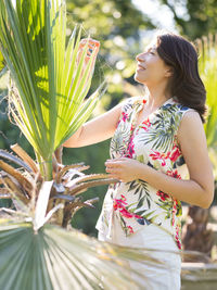 Caucasian woman is admiring of green foliage of palm trees in public park. summer vibes.