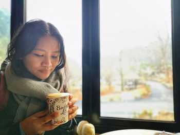 Woman holding coffee sitting by window in cafe