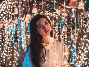 Portrait of young woman standing against illuminated lights