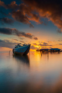 Boat moored in sea against sky during sunset