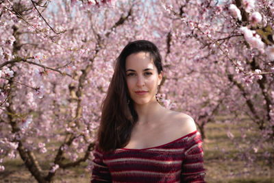 Portrait of beautiful young woman standing by cherry blossom tree