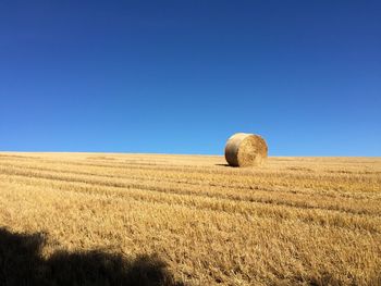 Hay bales on field against clear blue sky