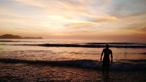 Rear view of silhouette man walking at beach during sunset