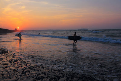 Silhouette people on beach against sky during sunset