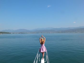 Rear view of woman with arms raised standing by railing against sea