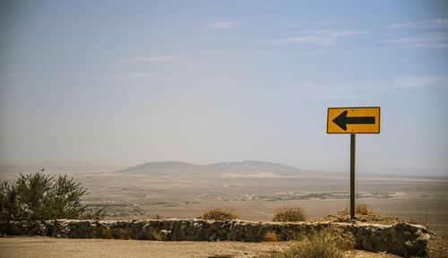 Road sign on field against sky