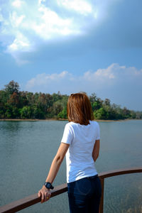 Rear view of woman standing by lake against sky