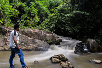 Full length of young woman standing by waterfall in forest