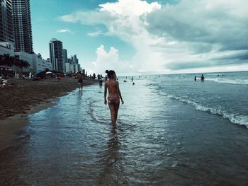 Rear view of woman wearing bikini while walking on beach against sky