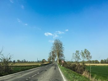 Empty road amidst field against blue sky