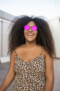 Young and afro woman with sunglasses laughing and smiling while looking at camera