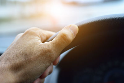 Cropped hand of man holding steering wheel while driving car