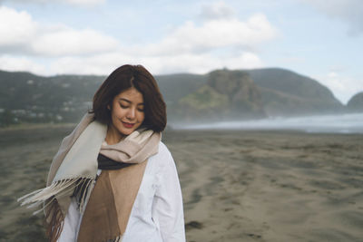 Young woman standing on beach against sky