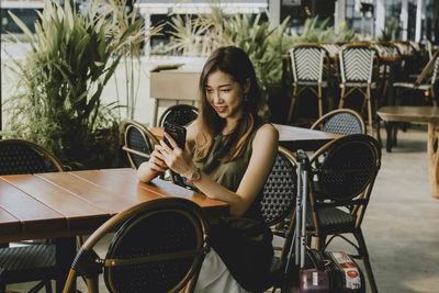 Young woman using smart phone while sitting on chair at outdoor cafe