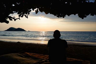 Rear view of silhouette man looking at sea during sunset