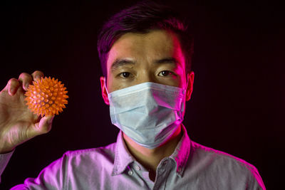 Portrait of young man holding flowers against black background