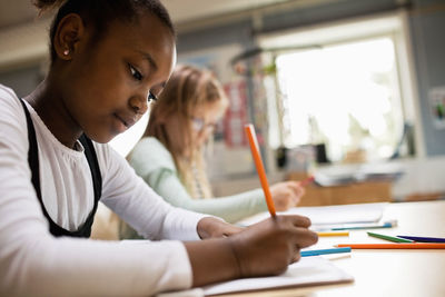 Concentrated girl writing while sitting at desk in classroom
