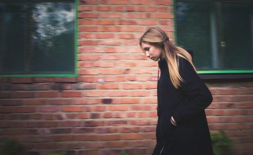 Side view of woman standing against brick wall