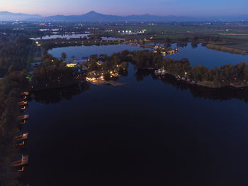 High angle view of illuminated city by lake against sky