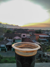 Close-up of coffee cup and buildings against sky