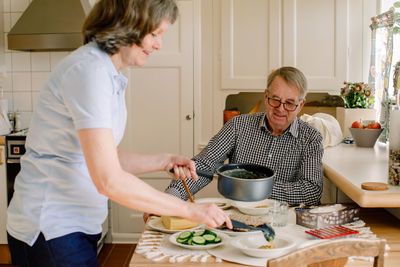 Side view of female caregiver is serving meal at table for retired senior man sitting in nursing home