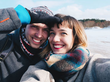 Close-up portrait of cheerful young couple against sea