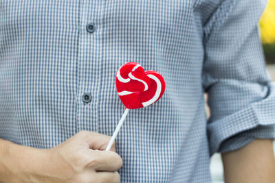 Midsection of man holding heart shape lollipop