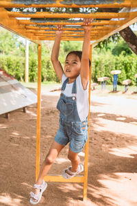 Full length of girl hanging on monkeys bars in playground