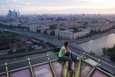 Man sitting on bridge over river against buildings in city