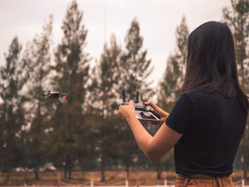 Rear view of woman flying drone against trees