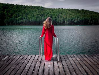 Rear view of woman wearing red dress standing on a wooden pontoon near the lake