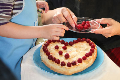 Midsection of people with raspberries and cake