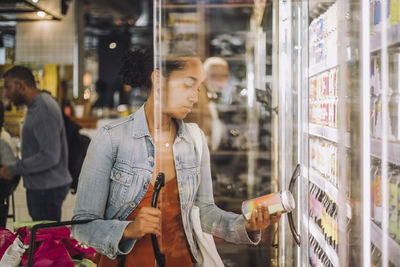 Female customer examining jar while standing at grocery store