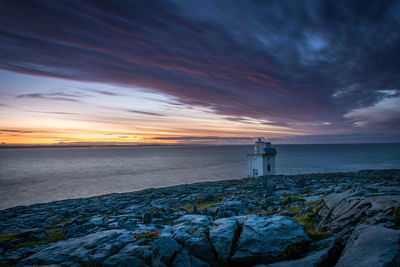 Lighthouse by sea against sky during sunset