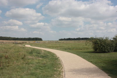 Empty road amidst field against sky