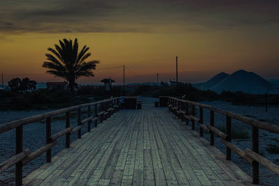 Footpath by sea against sky during sunset