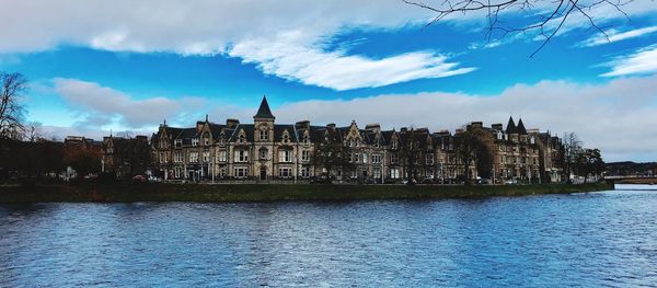 Buildings at waterfront against cloudy sky