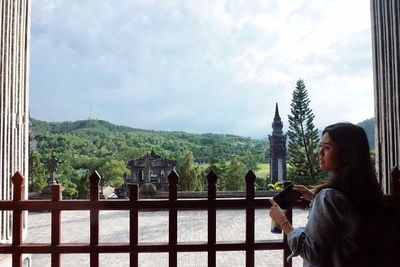 Woman sitting on railing against sky