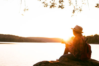 Man sitting by lake against sky during sunset