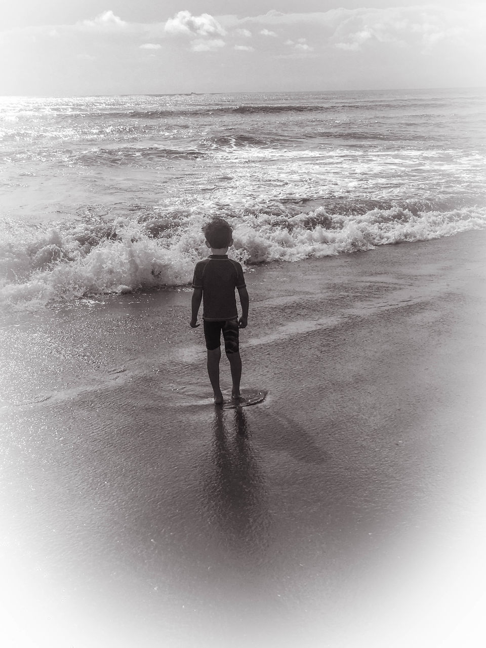 REAR VIEW OF BOY STANDING ON BEACH AGAINST SEA