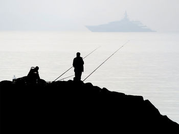 The fascinating silhouette of amateur fishermen on the rocks against the sky