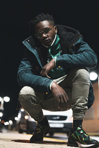 Full length portrait of young man crouching at night