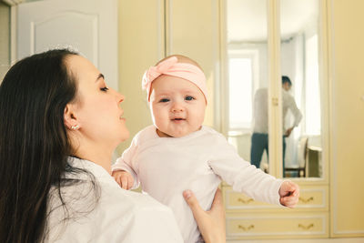 Mother holding daughter with reflection of father in mirror at home